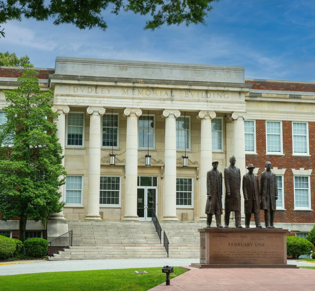 A photo of a statue of four individuals in front of a large white building with pillars.